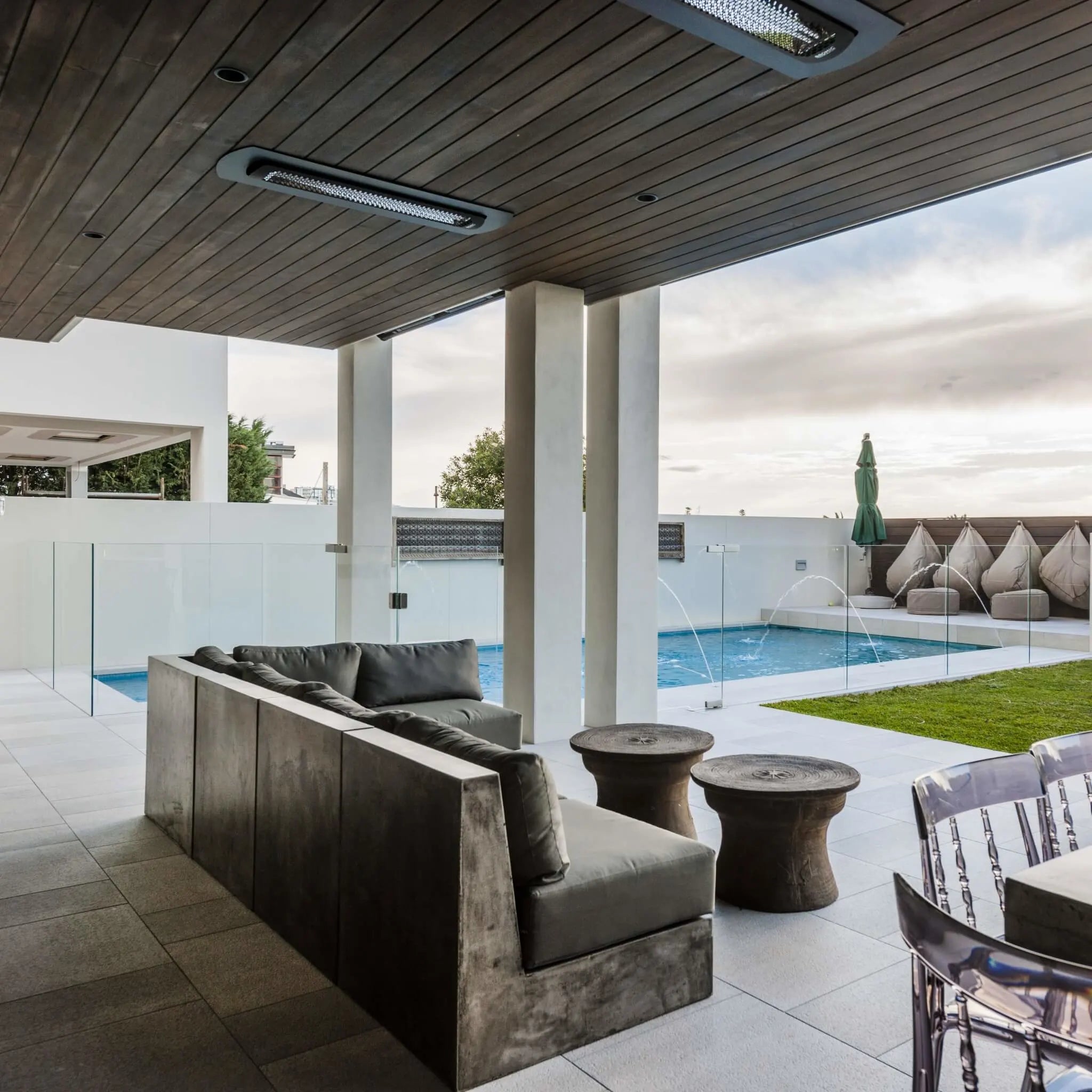 Modern covered patio with recessed Bromic Heating Tungsten Smart-Heat Electric Heaters in black, providing cozy warmth above a contemporary outdoor lounge and poolside seating area.