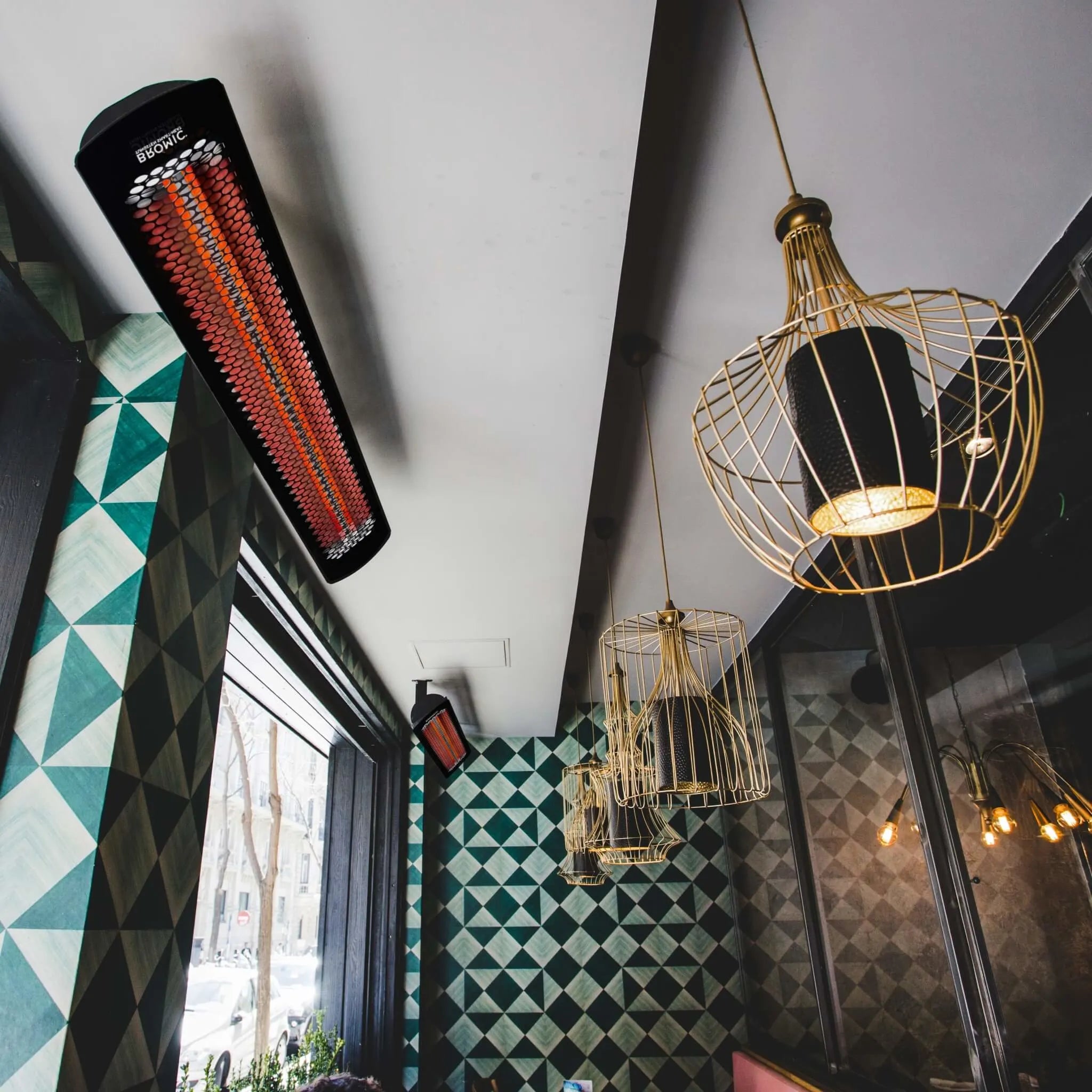 Contemporary restaurant interior with ceiling-mounted Bromic Heating Tungsten Smart-Heat Electric Heaters, blending radiant warmth with modern dÃ©cor and geometric wall patterns.