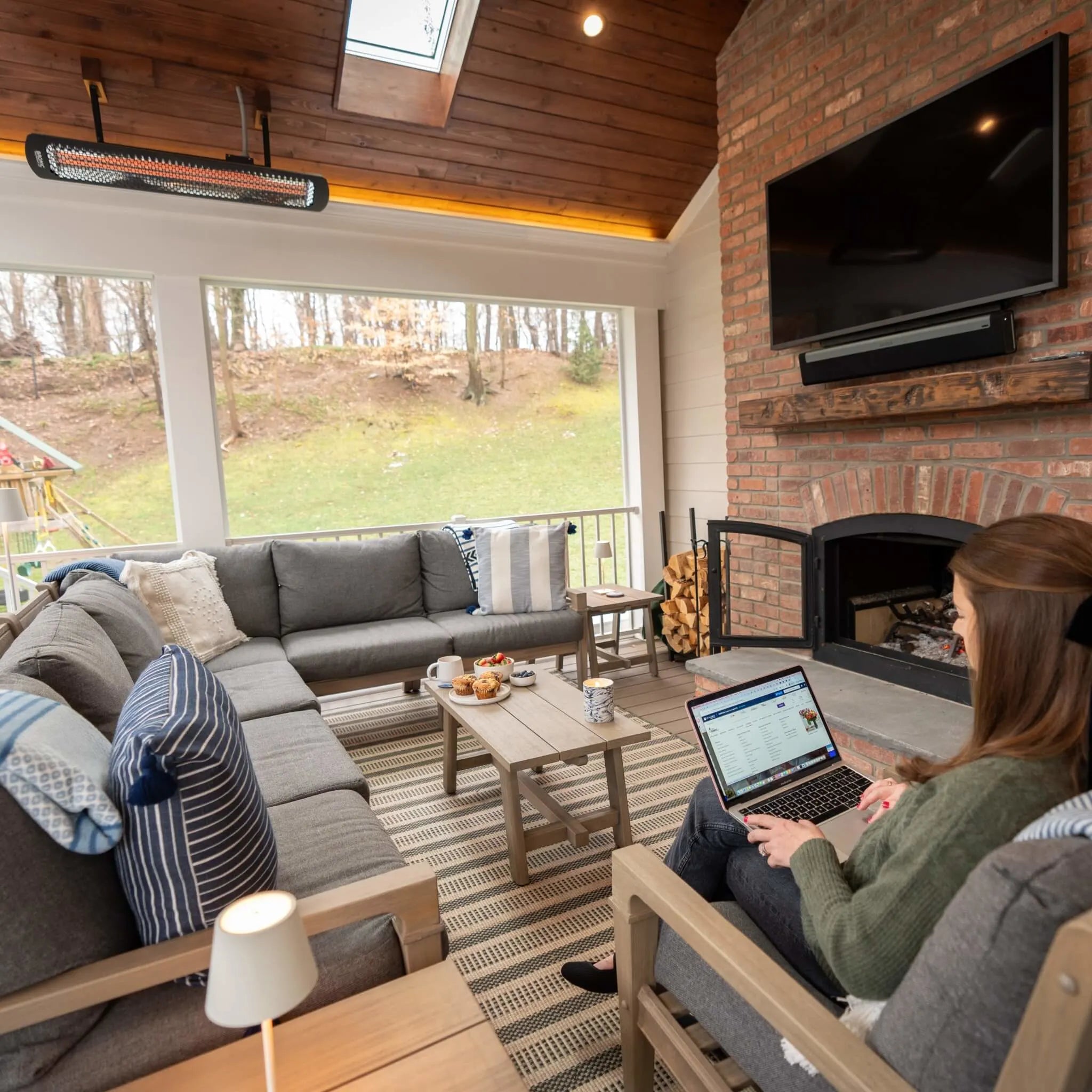 Warm, inviting screened porch featuring a Bromic Heating Tungsten Smart-Heat Electric Heater, comfortable sectional seating, and a wood-burning fireplace for year-round outdoor comfort.