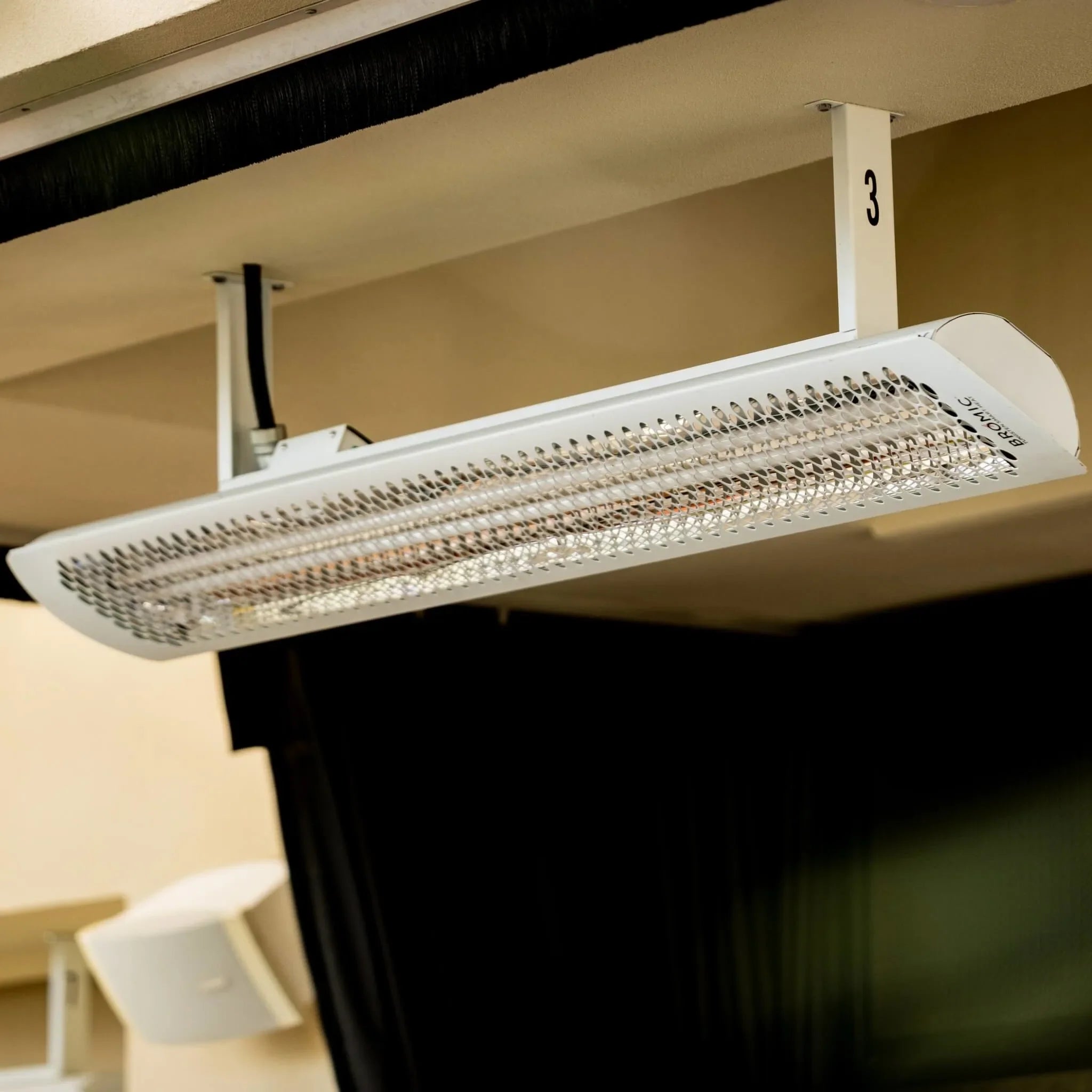 Guests enjoying drinks at a bar equipped with Bromic Tungsten Electric Smart-Heat heaters above, offering comfortable radiant warmth for year-round indoor-outdoor entertaining.