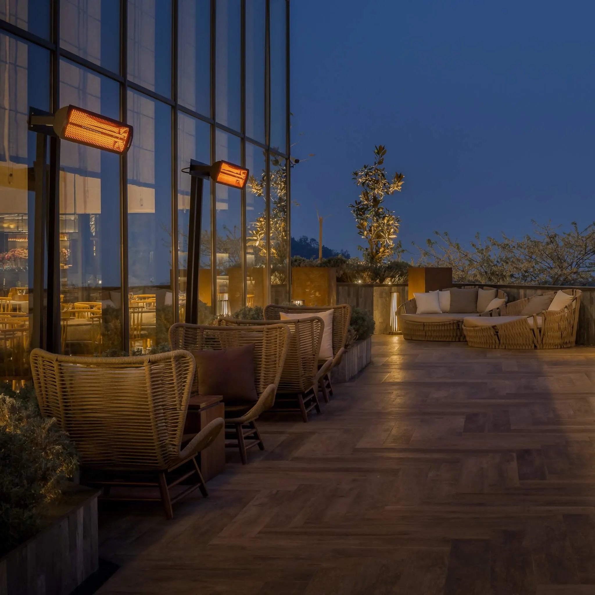 Rooftop dining area illuminated by multiple Bromic Tungsten Electric Smart-Heat heaters on post mounts, offering cozy warmth for guests enjoying the mountain view at dusk.