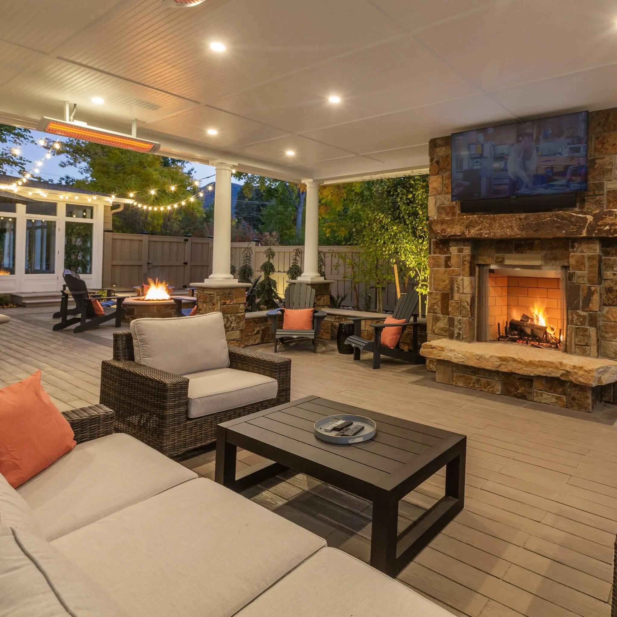 Covered patio featuring Bromic Tungsten Electric Smart-Heat black heaters mounted to the ceiling, providing cozy warmth for a stylish outdoor living area with a stone fireplace and TV.