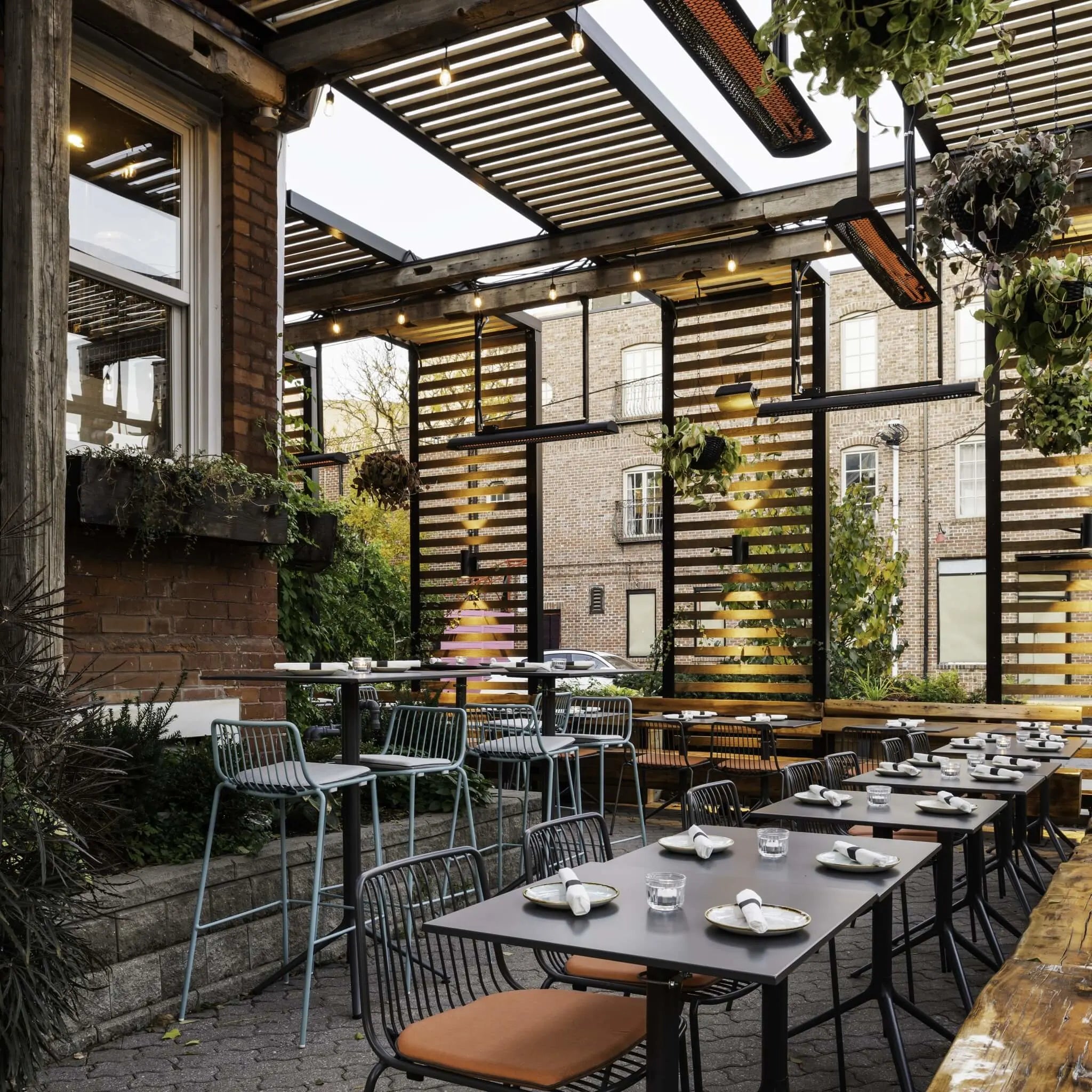 Rustic restaurant patio featuring Bromic Tungsten Electric Smart-Heat heaters mounted under a wood pergola, keeping guests comfortable in a cozy, plant-filled outdoor dining space.
