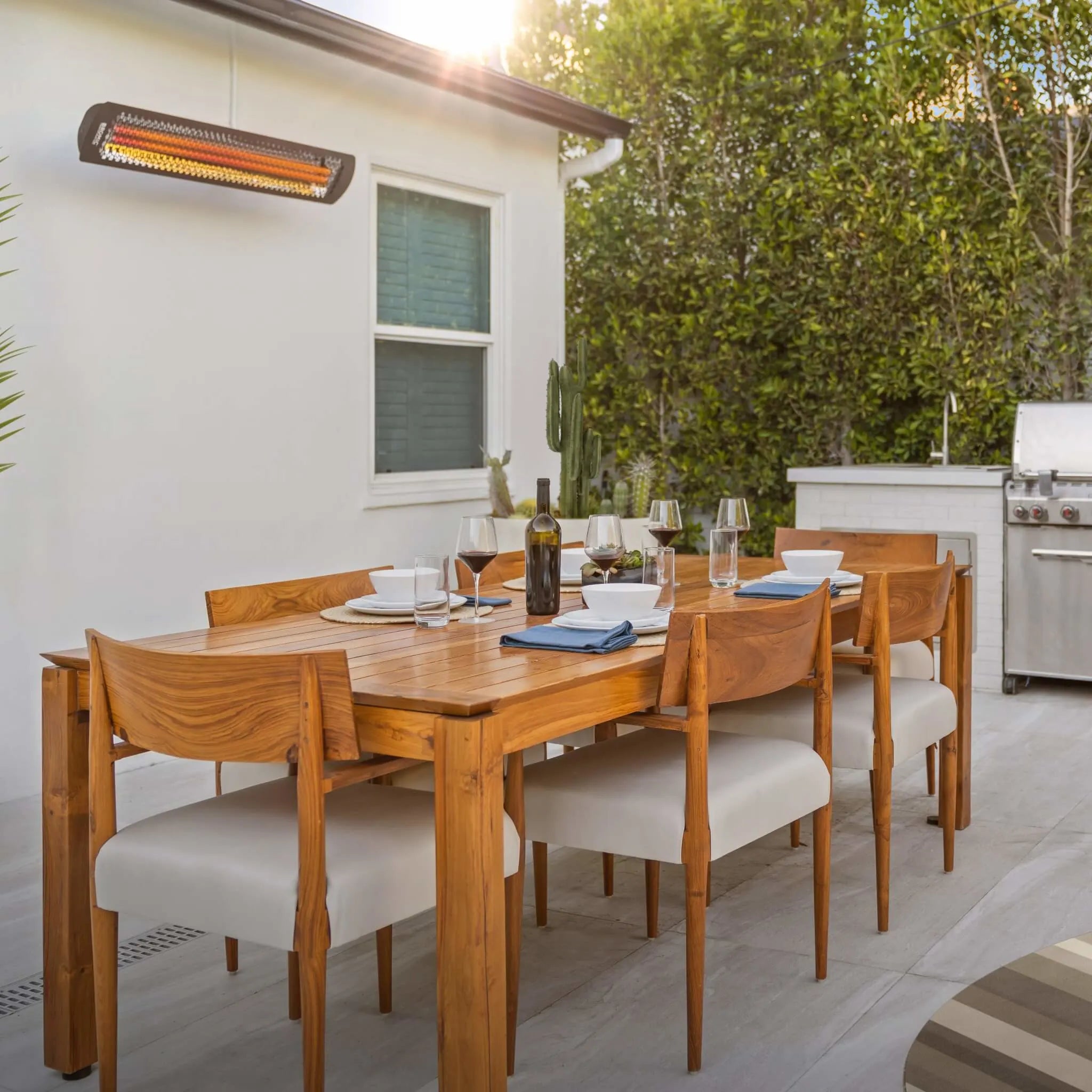 Modern residential patio with Bromic Tungsten Electric Smart-Heat heater mounted above a teak outdoor dining set, providing radiant warmth for family gatherings and outdoor meals.
