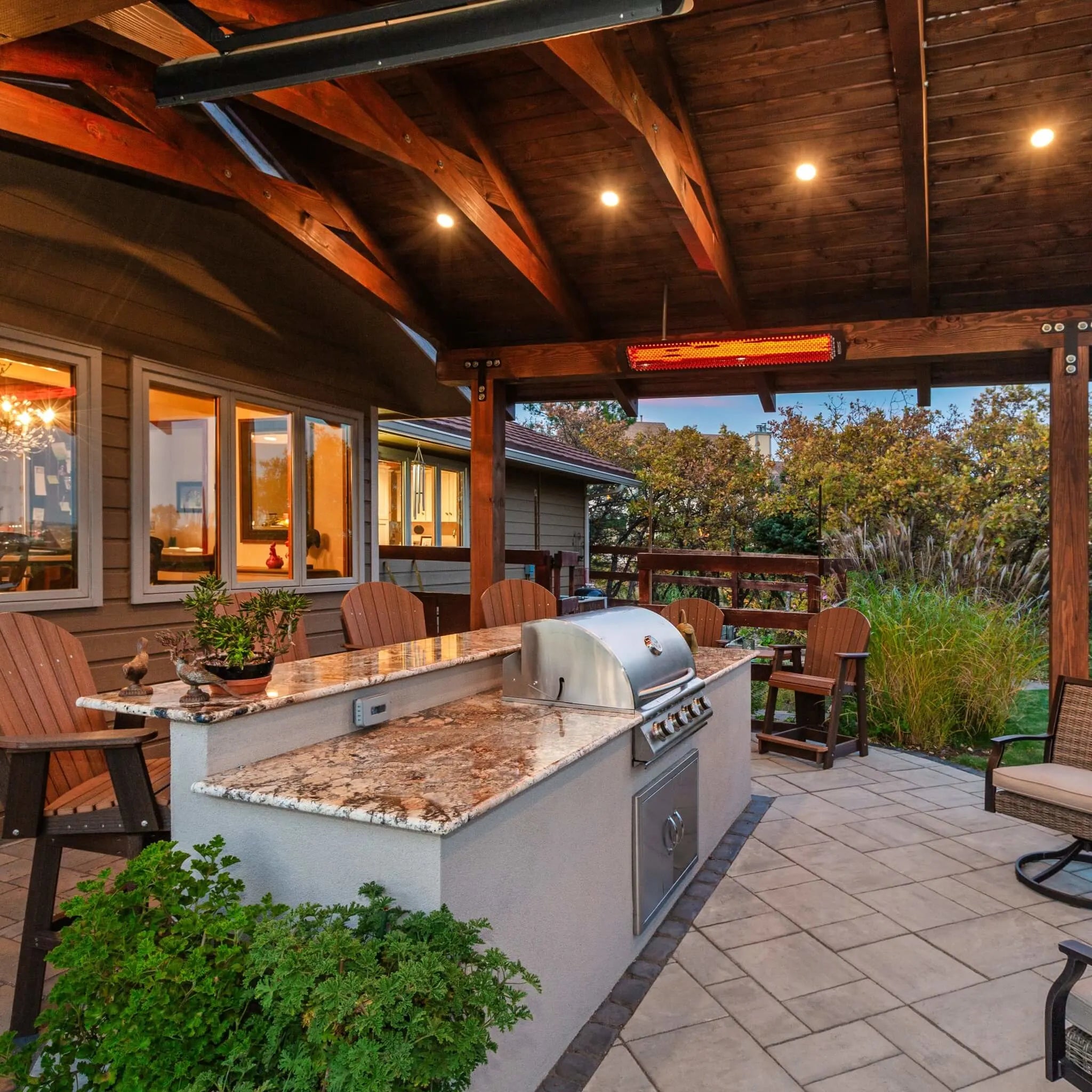 Outdoor kitchen and BBQ island under a wooden pergola, featuring Bromic Tungsten Electric Smart-Heat heaters to keep guests cozy during evening gatherings.