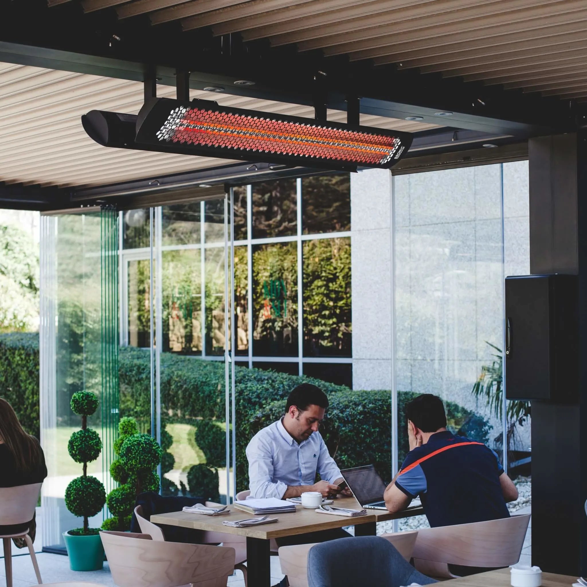 Contemporary commercial patio space with Bromic Tungsten Electric Smart-Heat heater installed overhead, creating a warm, inviting atmosphere for outdoor meetings and casual dining.