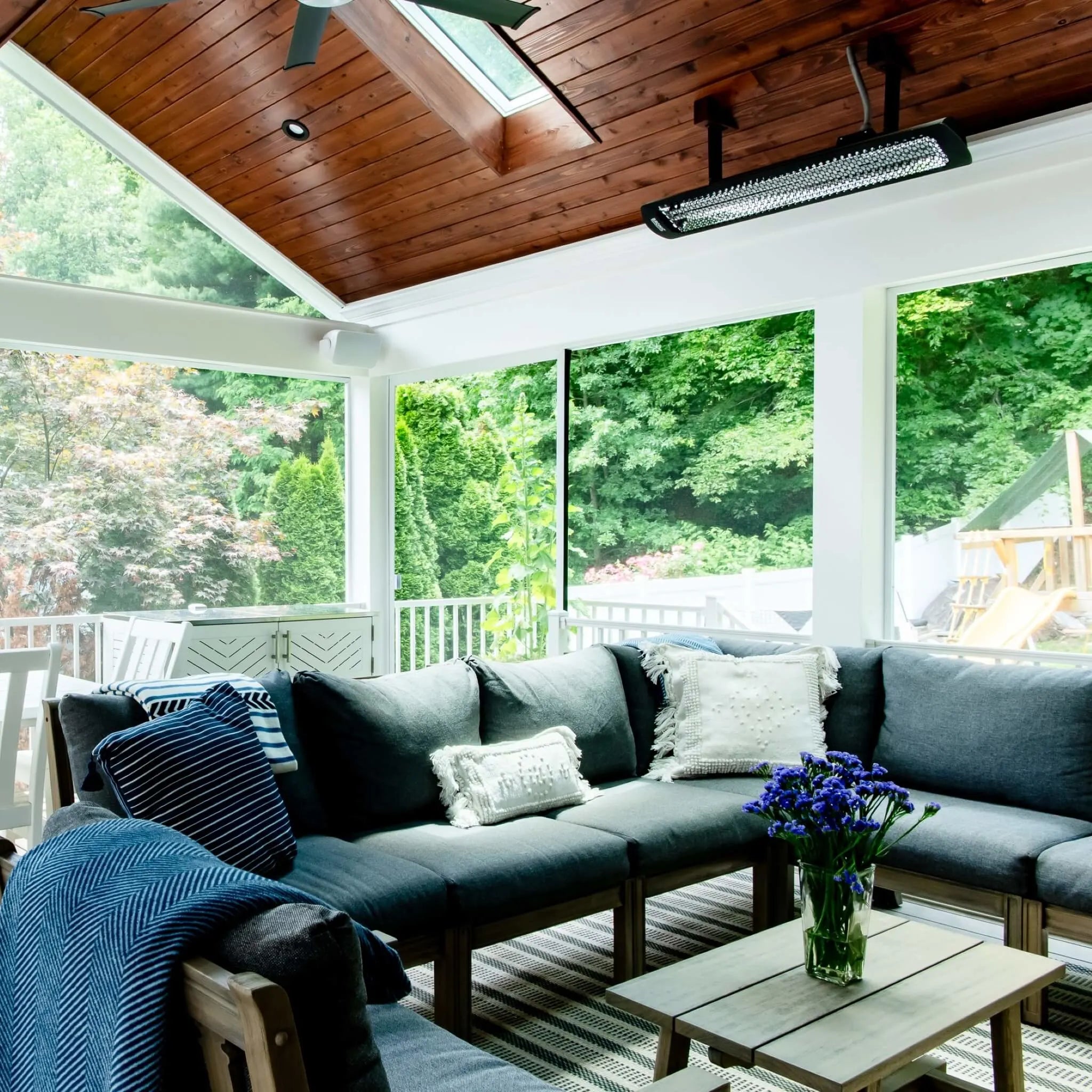 Bright enclosed patio with vaulted wood ceiling featuring a Bromic Tungsten Electric Smart-Heat heater, warming a cozy gray sectional seating area filled with natural light.