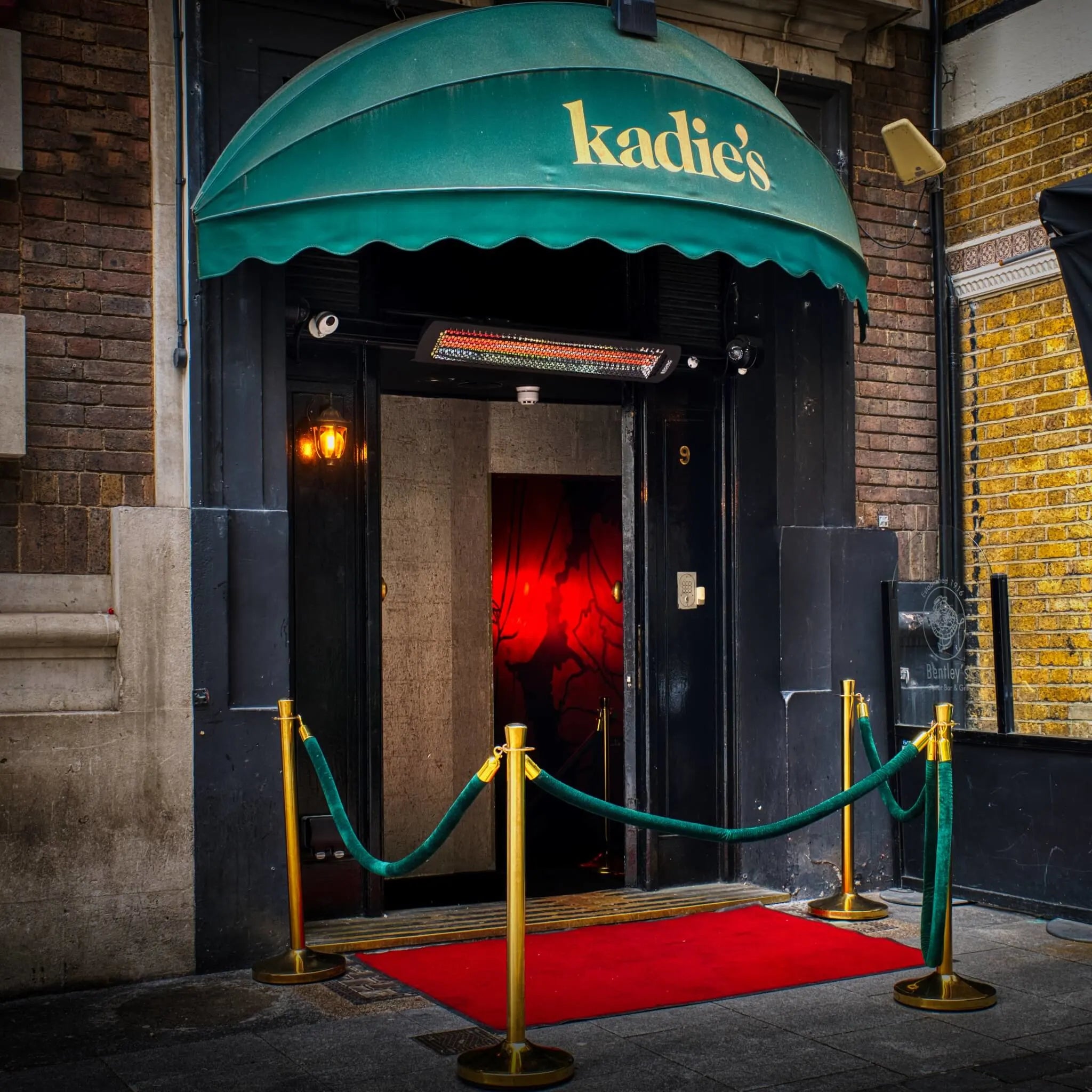 Elegant nightclub entrance in London with a Bromic Tungsten Electric Smart-Heat heater mounted above the door, warming the red-carpet entryway beneath a green awning.